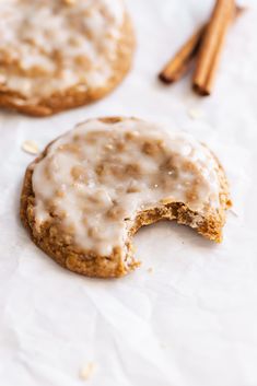 two cookies with icing and cinnamon sticks next to each other on white parchment paper