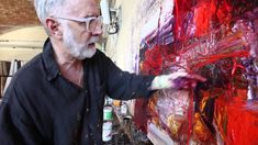 an older man is painting on a large piece of art with red and purple paint