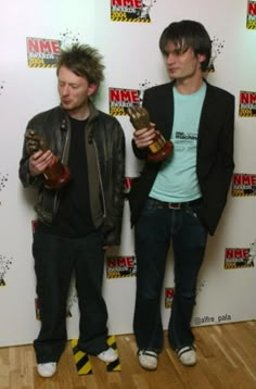 two young men standing next to each other holding trophies in front of a white wall