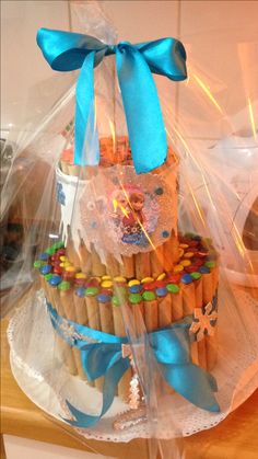 a cake made to look like a castle with blue ribbon and candy on top is wrapped in plastic