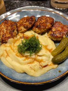 a blue plate topped with meatballs and mashed potatoes next to a pickle