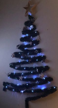 a christmas tree made out of black and blue tinsel with lights on it, hanging from the wall