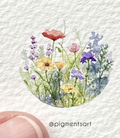 a hand is holding up a watercolor painting of wildflowers and poppies