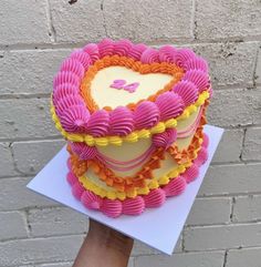 a heart shaped cake on top of a white plate with pink and yellow icing