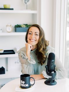 a woman sitting at a table with two coffee mugs in front of her smiling