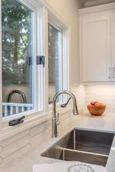 a bowl of fruit sitting on top of a kitchen counter next to a sink and window