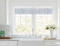 a white kitchen with blue and white roman shades on the window sill above the sink