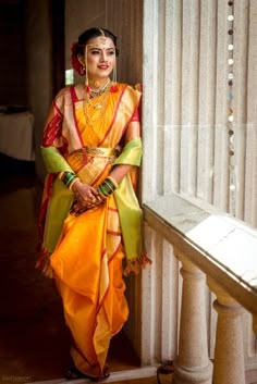 a woman in an orange and yellow sari standing next to a pillar with columns