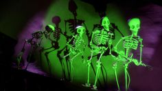 three skeletons standing in front of a green wall with purple light behind them and one skeleton sitting on top of the other