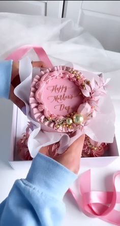 a person holding a pink birthday cake in a box with ribbon around it and the words happy mother's day written on it