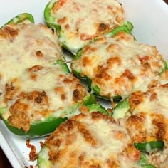 several stuffed peppers in a white dish on a wooden table with cheese and seasoning