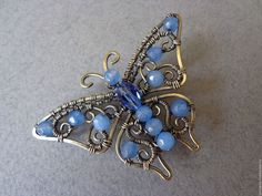 a brooch with blue beads on it sitting on a gray surface, in the shape of a butterfly