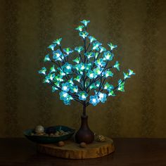 a lighted tree is sitting on a table next to a bowl with rocks in it