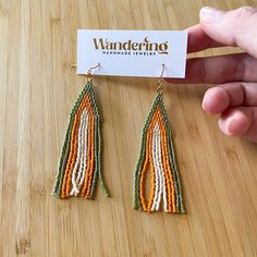 a pair of orange, white and green seed beaded earrings on a wooden table