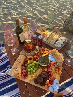 an assortment of food and wine on a picnic table at the beach