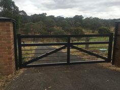 a gated driveway leading to a grassy field with trees in the distance and a brick wall on either side