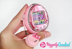 a hand holding a pink cell phone with a bow on it's strap and an embellishment in the middle