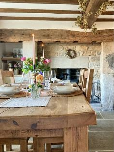 a wooden table with plates and glasses on it in front of a fireplace, surrounded by wood beams