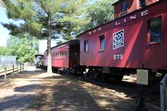 a red train car sitting on the tracks next to a tree and fenced in area