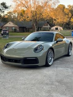 a silver sports car parked in front of a house next to a parking lot with trees