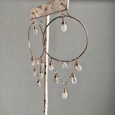 Details: ~Gold filled hand hammered hoops.~Hand wrapped rainbow moonstone gems.~Hanging cascading chain.~Hoops measure approximately 2" in diameter.~Earrings measure approximately 3 3/4” from the top of the hook to the bottom of the longest moonstone. These gorgeous handmade hoops add a touch of sophisticated glam to any outfit, from your wedding day to coffee dates with your girls! Love a certain stone? Well these beauties are fully customizable! I can create the Waterfall Hoops with the stone Dyi Earrings, Afro Jewelry, Stone Well, Hoop Earrings Diy, Boho Hoop Earrings, Plant Jewelry, Coffee Dates, Asymmetrical Earrings, Earrings Inspiration