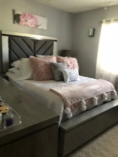 a bed with pink and white pillows on top of it next to a window in a bedroom