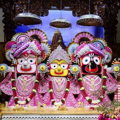 three colorfully painted masks are on display in front of a large screen with chandeliers hanging from the ceiling