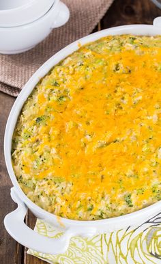 a casserole dish with cheese and broccoli in it on a wooden table