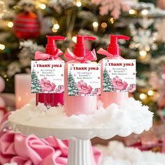 three pink hand soaps sitting on top of a white cake covered in snow next to a christmas tree