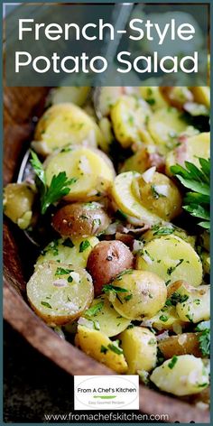 a wooden bowl filled with potatoes and parsley on top of a table next to a spoon