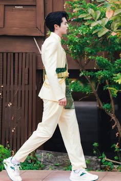 a man in a white suit is walking down the street with his hand on his hip