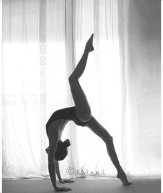 a woman doing a handstand in front of a curtain with her legs crossed