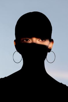 a woman's face is covered by a black veil with large hoop earrings on her head