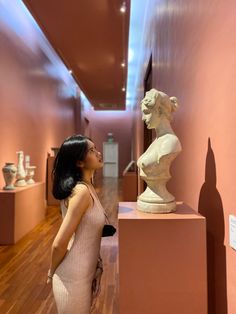 a woman looking up at a busturine on display in a room with pink walls