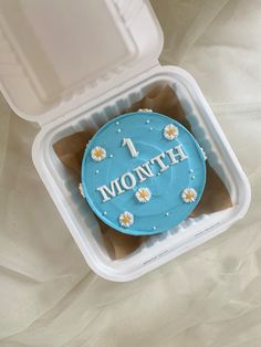 a blue cake in a plastic container with the word mom written on it and daisies