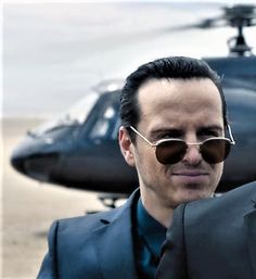 a man in a suit and sunglasses standing next to a helicopter