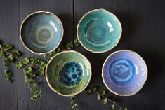 three blue and green bowls sitting on top of a wooden table next to some leaves