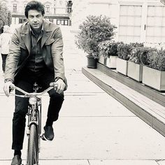 a man riding a bike down a sidewalk next to potted plants on either side