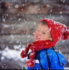 a young boy wearing a red hat and scarf in the snow with his mouth open