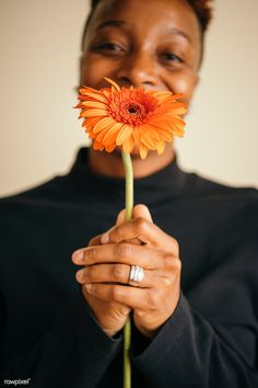 a woman holding an orange flower in front of her face