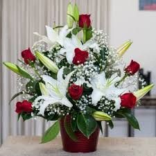 a vase filled with white lilies and red roses on top of a wooden table