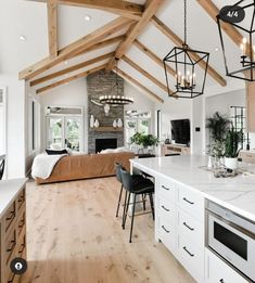 an open kitchen and living room with wood beams on the ceiling, white countertops and wooden flooring