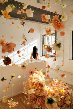 a woman is sitting in a room with flowers falling from the ceiling