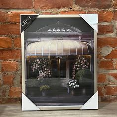 an image of a building with flowers in front of it on a table next to a brick wall