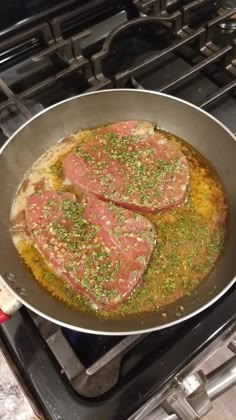 two pieces of meat are cooking in a pan on the stove top, with seasoning sprinkles