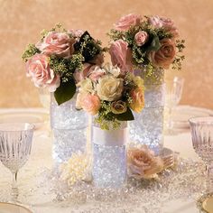 three vases filled with flowers sitting on top of a table next to wine glasses