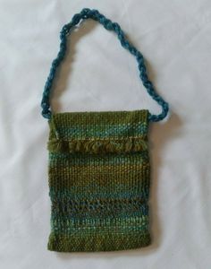 a green and blue knitted purse hanging on a white sheet with a string attached to it