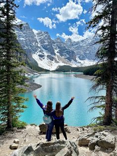 two women standing on top of a mountain with their arms in the air and mountains behind them