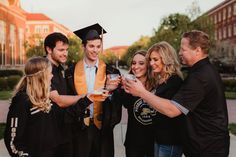 a group of people standing around each other in graduation gowns and holding drinks together