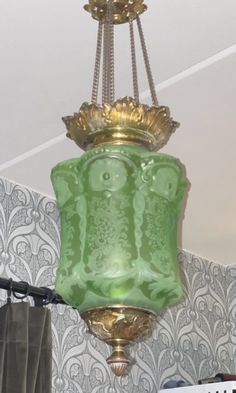 a green lamp hanging from the ceiling in a room with patterned wallpaper and curtains